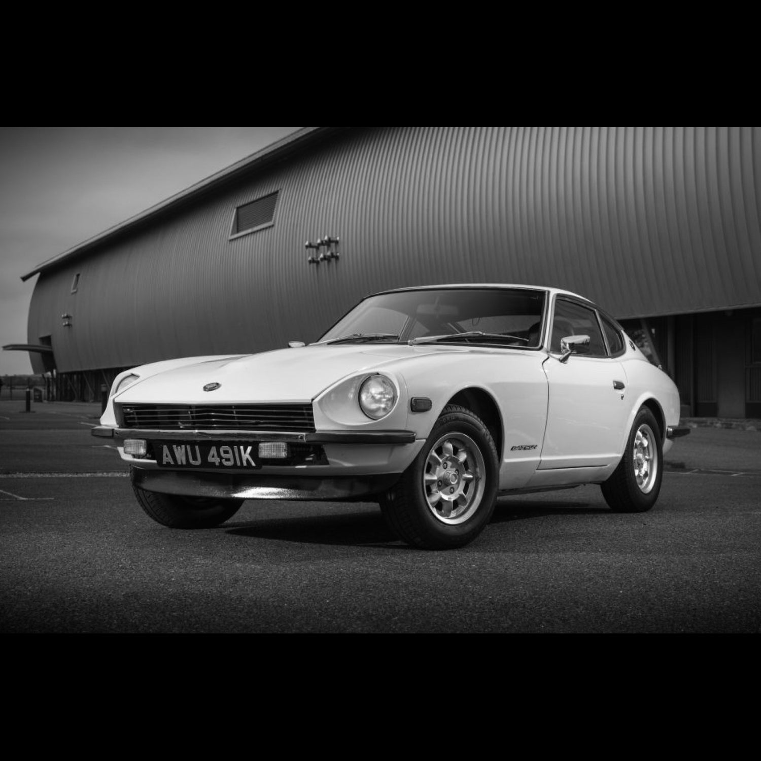 Nissan 240Z in front of a airplane hanger black and white